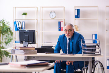 Old male employee in wheel-chair sitting in the office