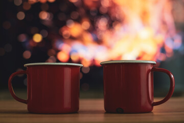 Two red enamel with a cup of coffee drink placed on wooden table. It was placed next to the campfire to cool down in the winter forest.