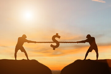 Silhouette of two young businessmen pulling tug of war with a rope on top of the mountain with sunset background. Concept for business competition, rivalry, challenge or dispute