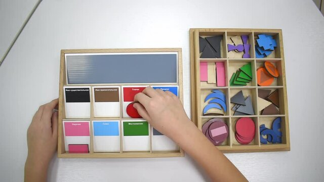 Top view of girls hand is playing and sorting a puzzle of colored wooden geometric shapes in montessori school. Concept of using learning resources for children education language and writing.