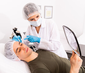 Skilled woman beautician examining face skin of male client in medical esthetic office