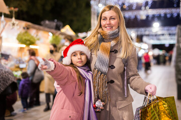 Mom and daughter point to Christmas decorations, choose and buy at the Christmas market