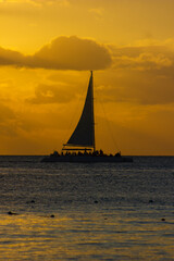 SUNSET ON THE BEACH WITH BOATS IN THE ORIZON AND ORANGE SUNLIGHT, WITH BLUE SKY AND SOME CLOUDS