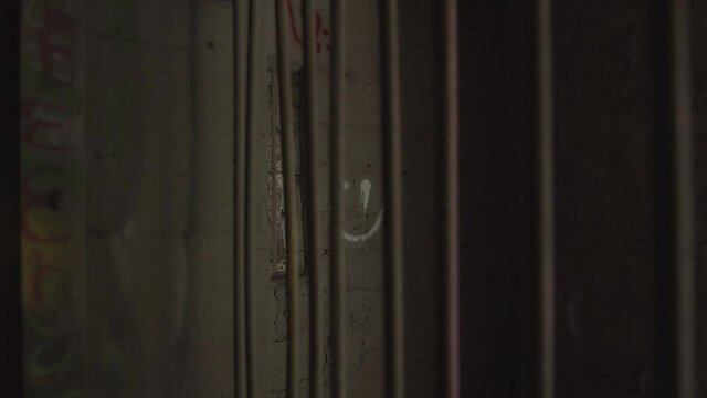 Pull back from within cage with smiley face painted on a wall, behind rusty bars, inside an abandoned building