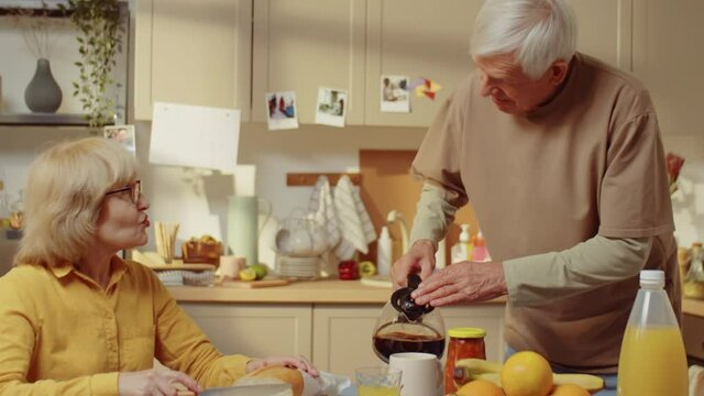 Senior Man Spending Morning With His Wife At Home Making Coffee Drink For Breakfast And Talking About Something