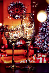 A wine glass and a champagne glass filled with shining lights of garlands. Shining glasses with bright lights create a festive atmosphere and a desire to celebrate Christmas and New Year.