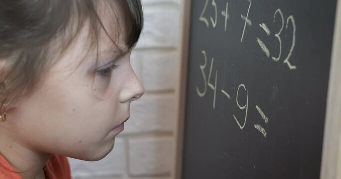 Schoolgirl doing exercise. A child think about her math exercises on the blackboard in the room.