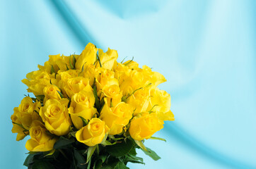 A bouquet of many delicate, yellow roses on a wavy, textured, blue, silk background.