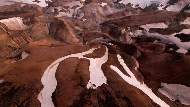Panning up aerial shot reveals truly beautiful Icelandic landscape with snowy mountains and fog/clouds. Shot in the highlands of Iceland, geothermal area below.