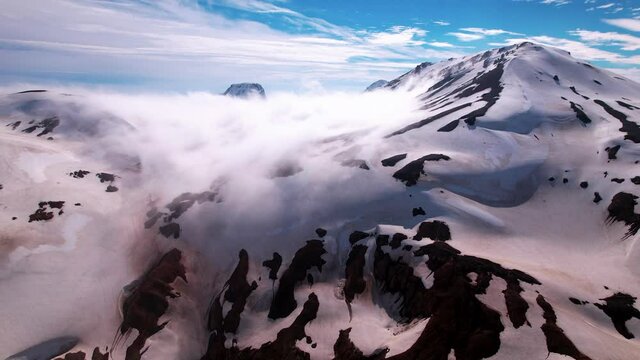 Incredible turning aerial shot high up in Icelandic snowy mountains. Fog and clouds with mountain peaks sticking out. 