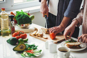 Angle view of couple's hands preparing the meal, chopping bread for sandwiches in their kitchen. Vegetarian healthy food. Healthy vegetarian lunch. Family