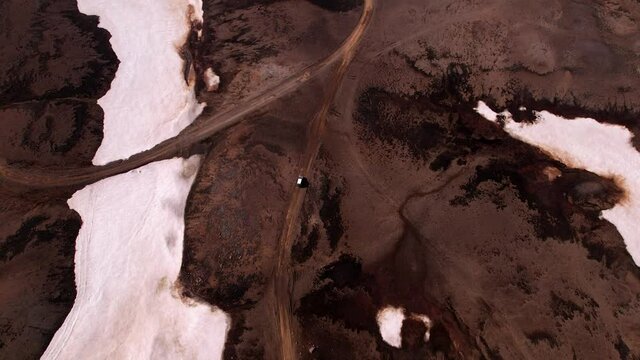 Aerial birds eye view following a vehicle traveling on a dirt road on the edge of snow. Shot in Iceland.