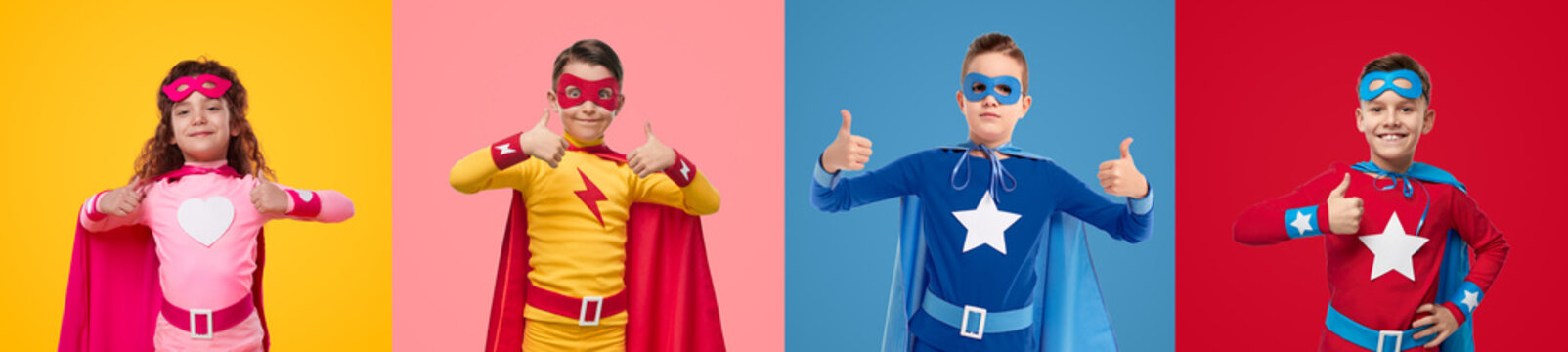 Cheerful kids in superhero costumes showing thumbs up