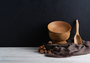 Wooden bowls and cutting boards on a wooden shelf against a rough plaster of a black wall. Rustic kitchen utensils.