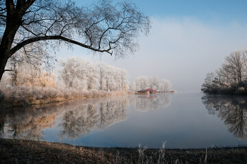 House by the lake. The transition of nature from autumn to winter. Foggy and sunny morning on the lake.