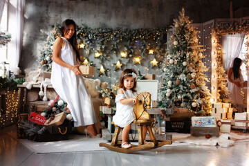 Obraz na płótnie Canvas The concept of family, winter holidays and people. A young mother and her daughter are happily playing on Christmas eve in a beautifully decorated room.