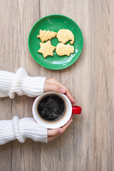 Merry Christmas with woman hand holding coffee cup and homemade cookie on table. Xmas eve, party, holiday and happy New Year concept