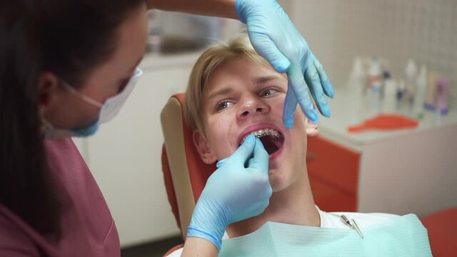 Teenager visits orthodontist. Careful lady dentist puts aligners on smiling teen schoolboy teeth to try on at appointment in professional clinic spbd