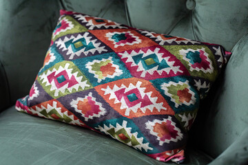 A bright decorative pillow with a geometric design on a green armchair.