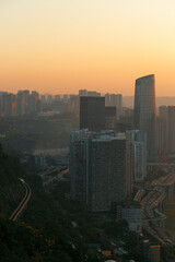 A city view at sunset, here in Chongqing, China. Next to the skyscrapers is the city transportation track, and in the distance is the silhouette of the sun setting over the mountains