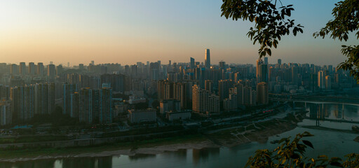 Obraz premium At sunset, in Chongqing, China, on the bank of the Jialing River, densely packed with high-rise buildings and bridges over the river, the afterglow of the setting sun falls on these buildings.