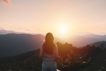 Happy young woman traveler relaxing and looking at the beautiful sunset on the top of mountain