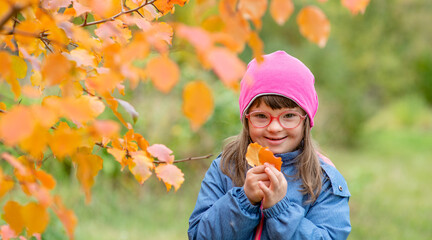 Smiling young girl with Downs syndrom holds autumn leaves. Empty space for text