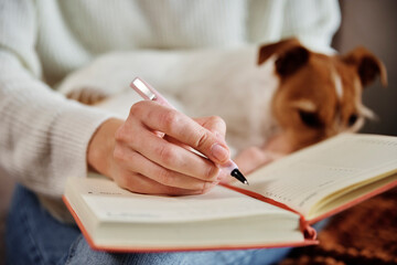 Woman working at home with her dog. Female hand write notes in notebook