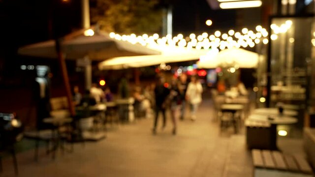Blurry image of people walking along night cafe lit up bokeh outdoors, alleyway