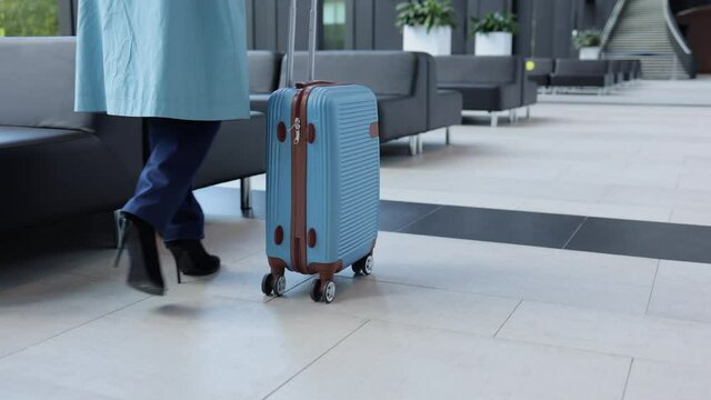 Young woman passenger moving suitcase and walking in airport building before of business trip spbi. Close-up view of stylish businesswoman walks confidently and holds luggage in hand, steps inside