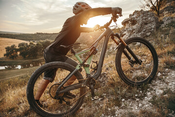 Young male cyclist rolling bike on grassy mountain slope in sundown