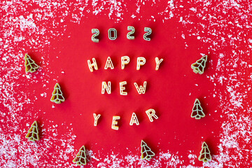 Lettering 2022 Happy New Year and christmas trees made of raw wheat pasta on a red background. Salt as snow. Flat lay, top view. Winter art food concept.