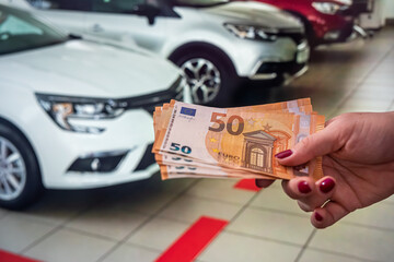 beautiful hand willingly holds new euro banknotes on a background of beautiful new cars.