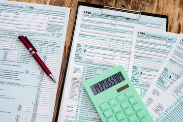 new tax forms 1040 usa with a green calculator with a red pen scattered on a wooden table