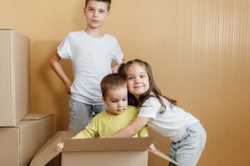 A friendly family of children of boys and girls is playing and rejoicing at moving to a new apartment against the background of cardboard boxes. Purchase of real estate. Housewarming, delivery.