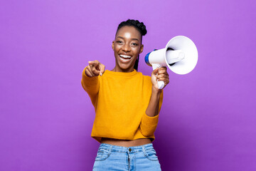 Smiling African American woman holding megaphone and pointing finger in isolated purple studio...