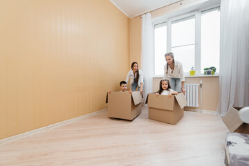 Moms are pushing their little kids to race, sitting inside cardboard boxes and having fun riding in the living room. Mortgage loan, the concept of home improvement. Housewarming.