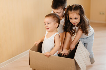 A friendly family of children boys and girls play and roll around each other in a cardboard box, rejoice at moving to a new apartment against the background of cardboard boxes.Transportation of goods.