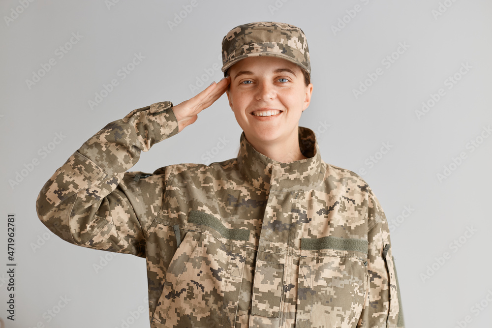 Wall mural extremely happy woman soldier with toothy smile and optimistic emotions saluting while standing agai - Wall murals