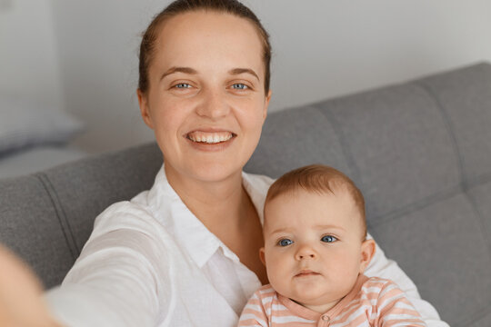 POV of smiling young adult mother and little baby, family using smart phone for making selfie, mom making images of with her cute toddler daughter, expressing happiness.