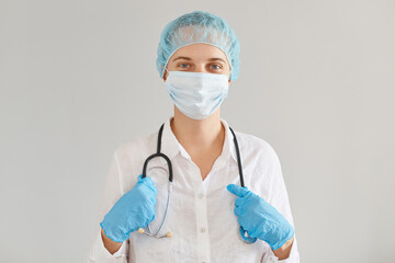 Fototapeta premium Positive medical doctor woman in the clinic, standing and keeping hands on her stethoscope, looking at camera, treating patients suffering covid or other illnesses.