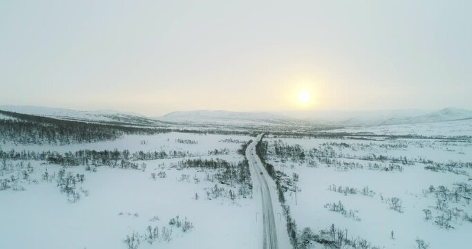 Cars driving on mountain road in arctic vinter landscape towards sunset