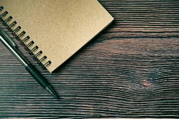 Notebook and pen placed on a brown wooden plank