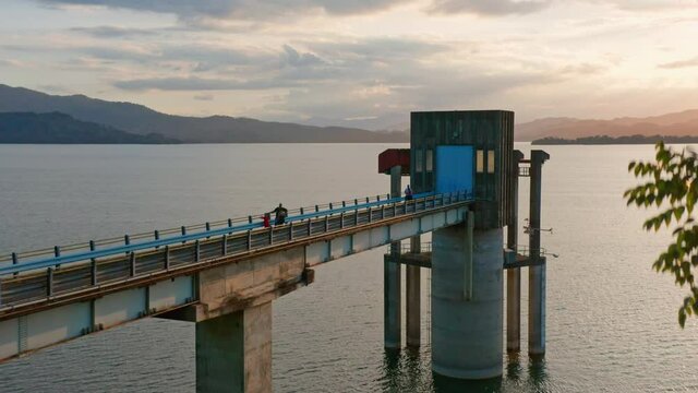 People At Bridge Connecting To Intake Tower At Hatillo Dam During Sunset. - aerial ascend