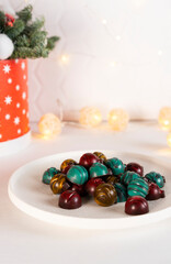 Green, yellow and red homemade chocolate candies in the shape of Christmas balls bauble on a white plate. Vertical orientation. Selective focus.