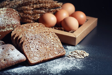 Fresh loaves of bread with wheat and gluten on a black table. Bakery and grocery concept. Fresh, healthy sorts of rye and white loaves food closeup. Fresh homemade bread with cereals.