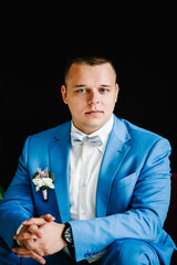 Wedding. The groom in a shirt, bow-tie and a suit with a buttonhole on black wall background. Rich...