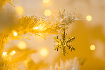 Close up of gold snowflake toy and garlands on white yellow Christmas tree