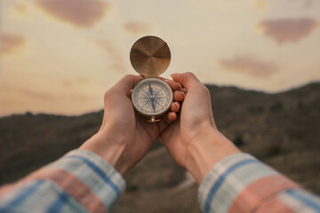 Travel concept. Vintage compass in female hands in the mountains during sunset.