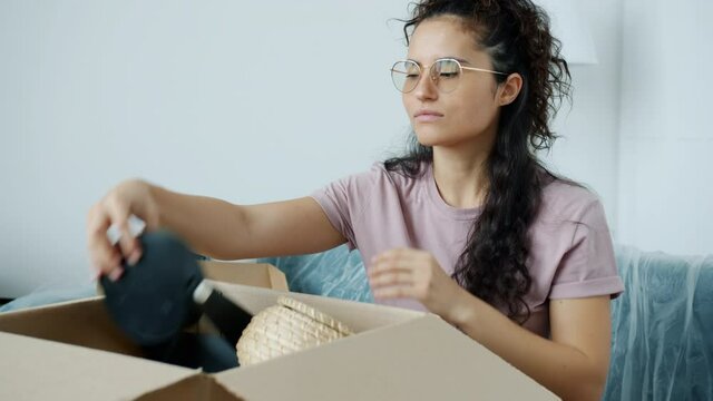 Slow motion portrait of attractive mixed race girl going through personal stuff unpacking box after relocation to new house. Modern people and accommodation concept.